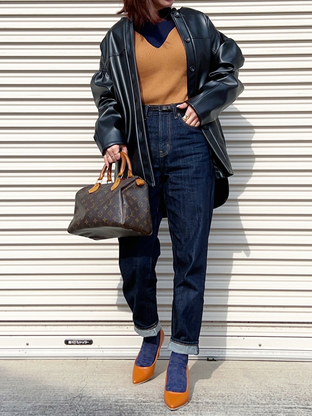 ブラック系のブルゾン、ベージュ系のニット/セーター、ブルー系のデニムパンツを着用したレディースの春コーディネートの2枚目の写真