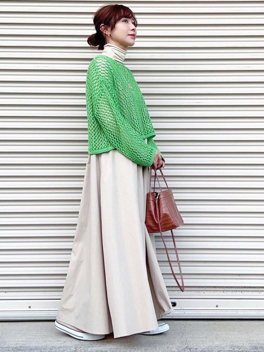 ベージュ系のワンピース、グリーン系のトップス、ベージュ系のスニーカーを着用したレディースの春コーディネートの2枚目の写真