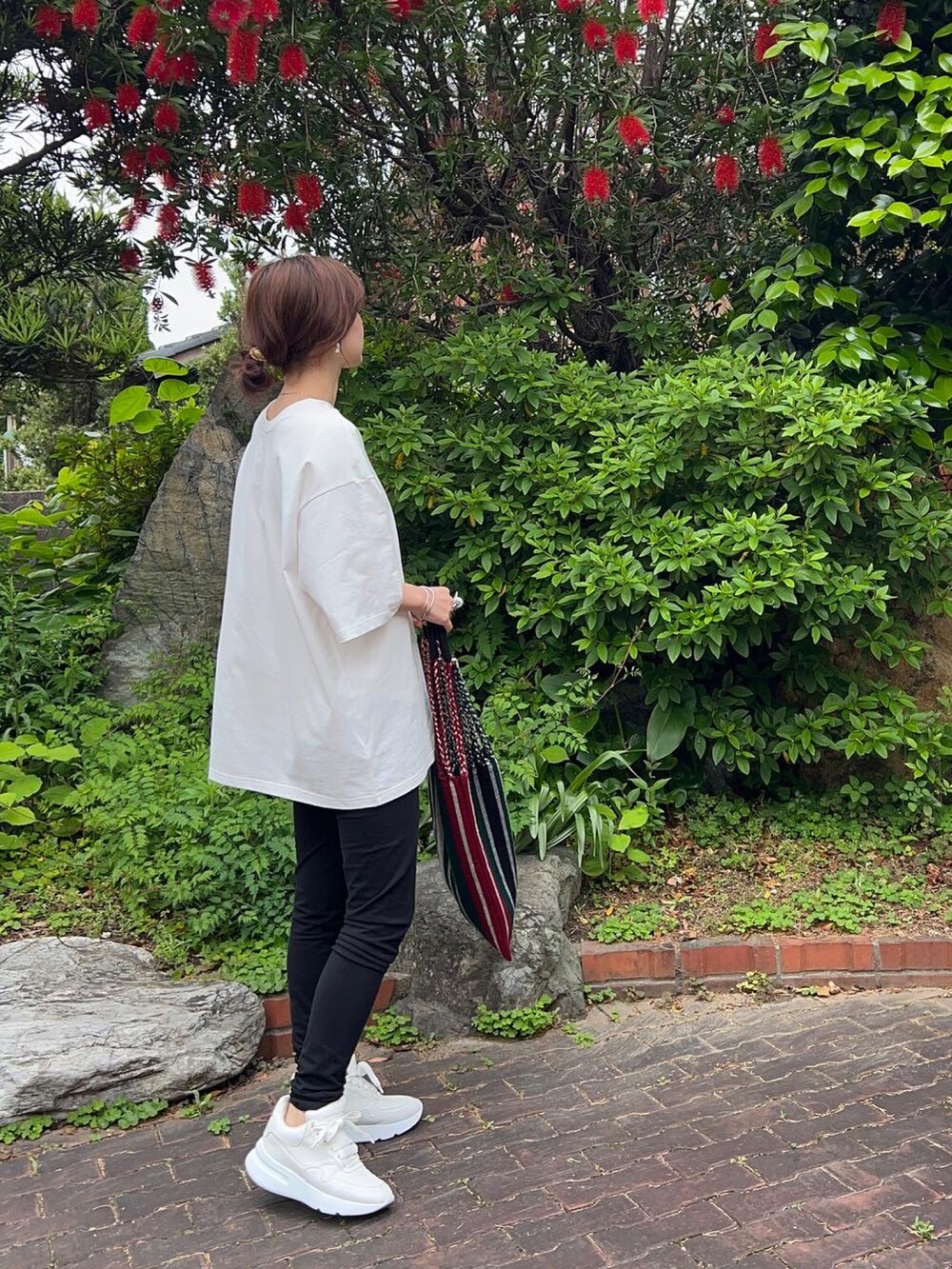 レッド系のトートバッグ、ホワイト系のTシャツ/カットソー、ホワイト系のスニーカーを着用したレディースの春コーディネートの2枚目の写真