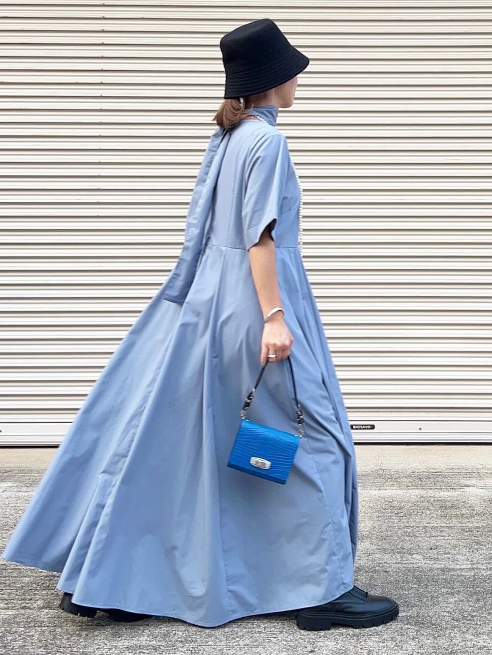 ブルー系のハンドバッグ、ブルー系のワンピース、ブラック系のブーツを着用したレディースの秋コーディネートの2枚目の写真