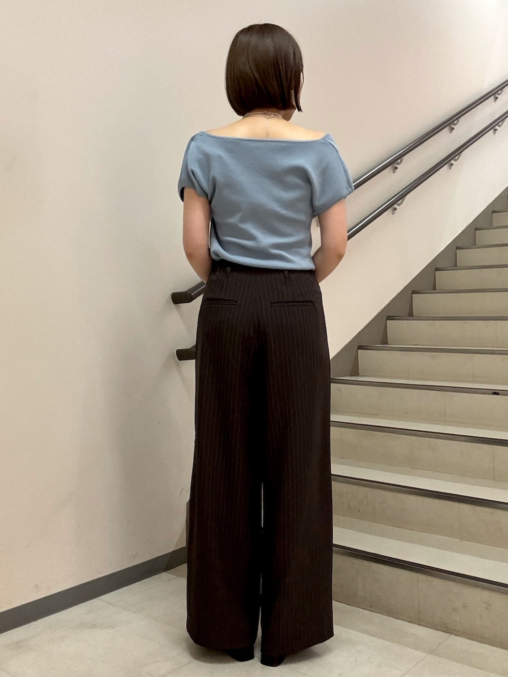 ブルー系のニット/セーター、ブラウン系のスラックス、ブラック系のショルダーバッグを着用したレディースの夏コーディネートの3枚目の写真