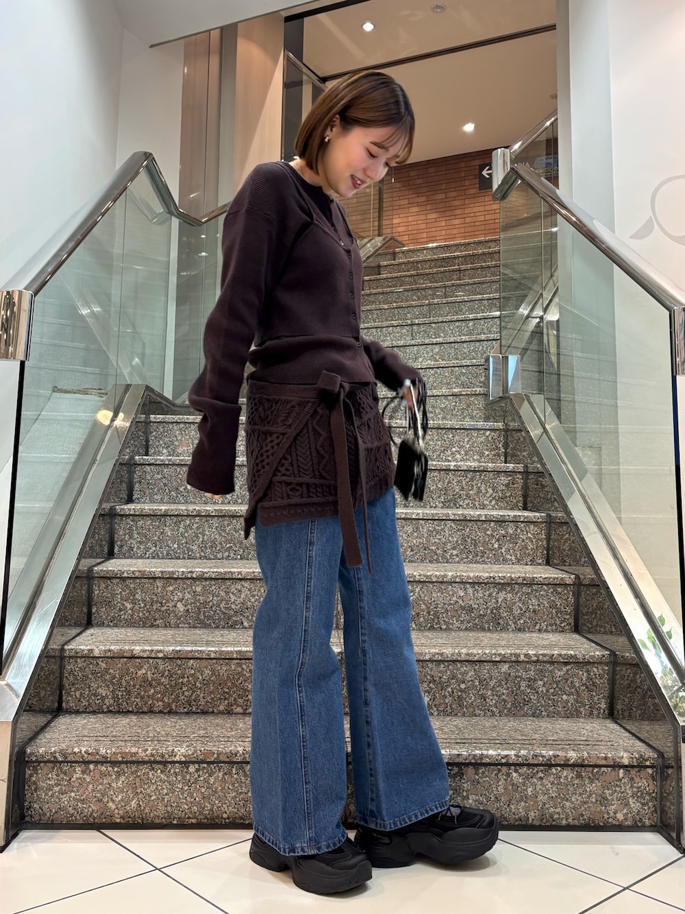 ブラウン系のニット/セーター、ブラウン系のスカート、ブルー系のデニムパンツを着用したレディースの冬コーディネートの5枚目の写真