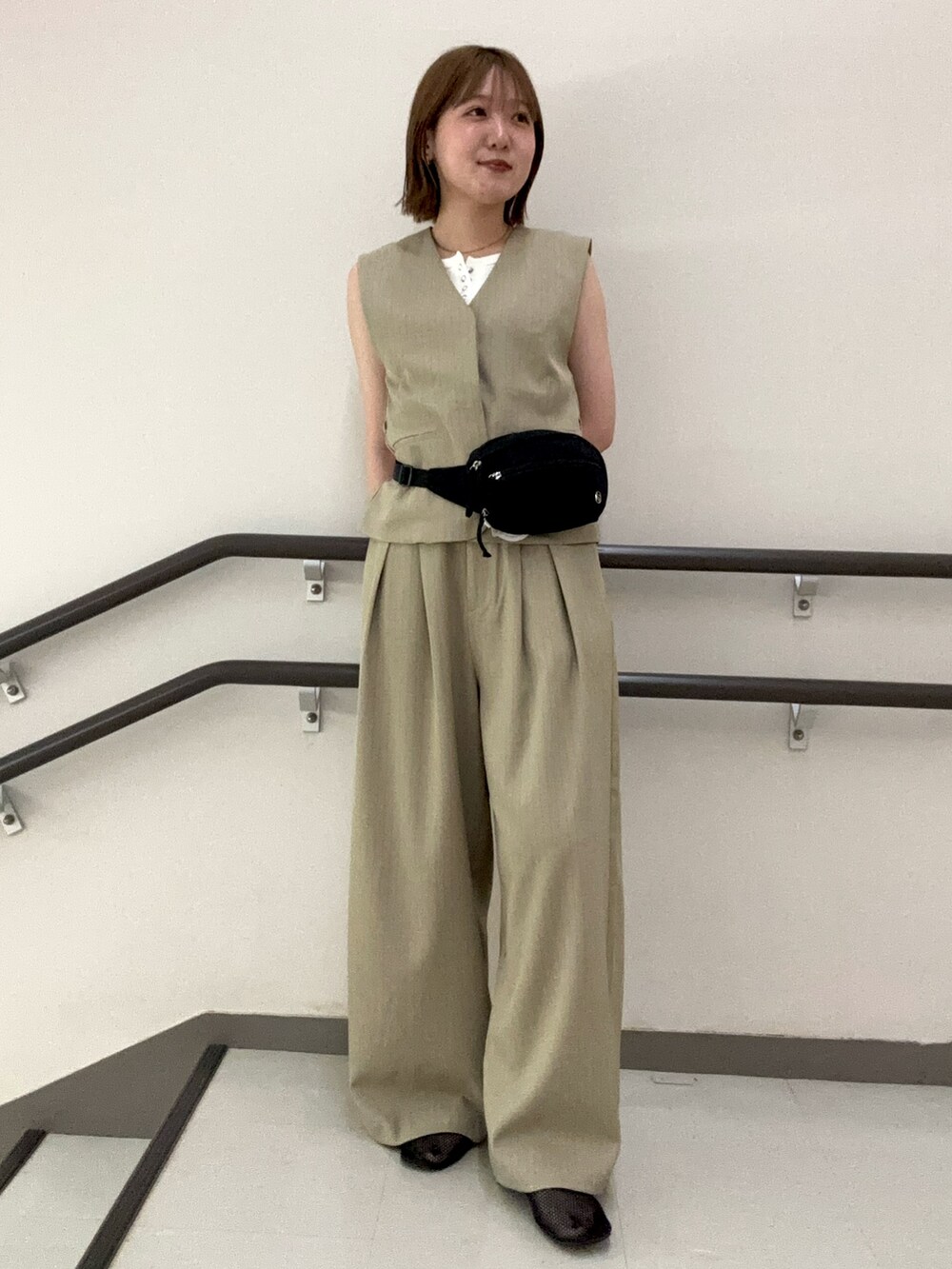 ベージュ系のスラックス、ベージュ系のベスト、ホワイト系のタンクトップを着用したレディースの夏コーディネートの2枚目の写真