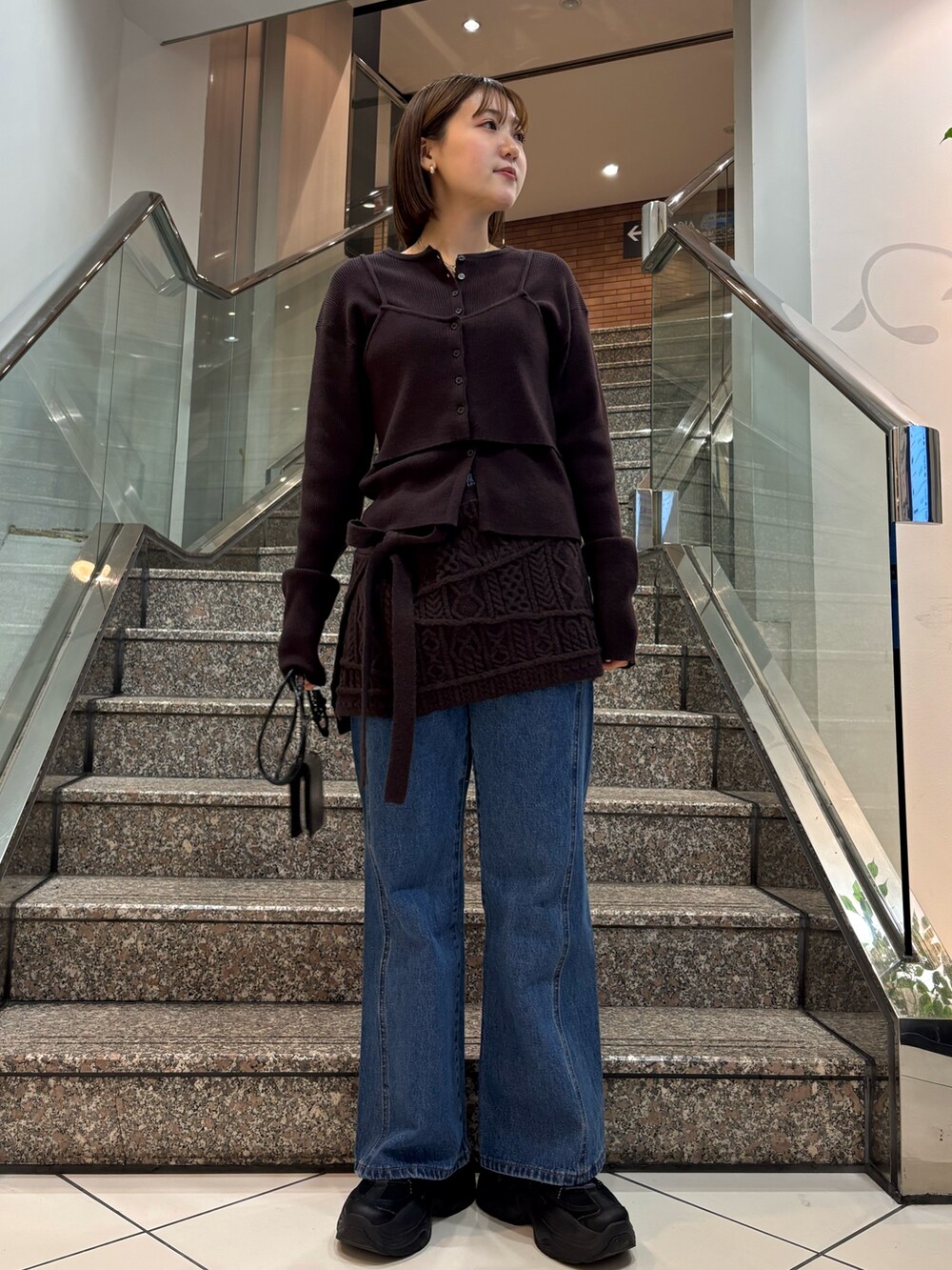 ブラウン系のニット/セーター、ブラウン系のスカート、ブルー系のデニムパンツを着用したレディースの冬コーディネートの2枚目の写真