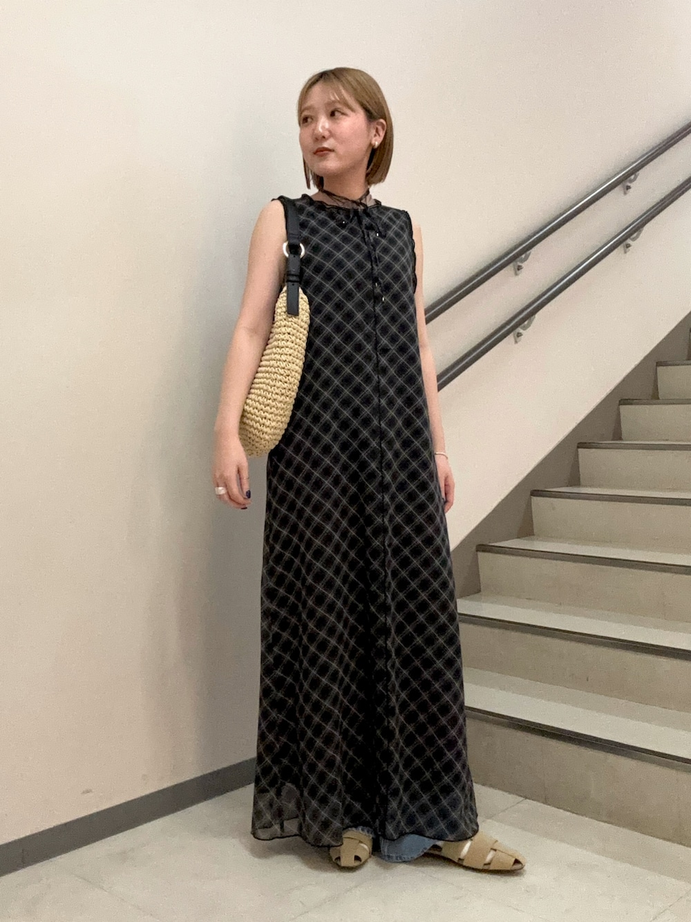 ブラック系のワンピース、ベージュ系のサンダル、ブルー系のデニムパンツを着用したレディースの春コーディネートの2枚目の写真