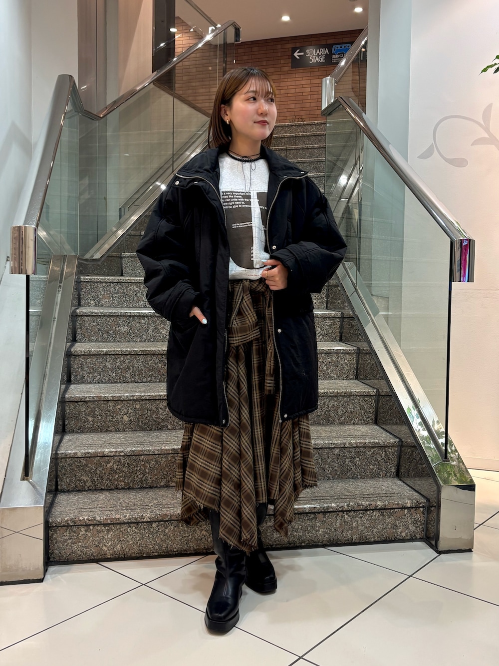 グレー系のTシャツ/カットソー、ブラウン系のスカート、ブラック系のダウンジャケット/コートを着用したレディースの冬コーディネートの2枚目の写真