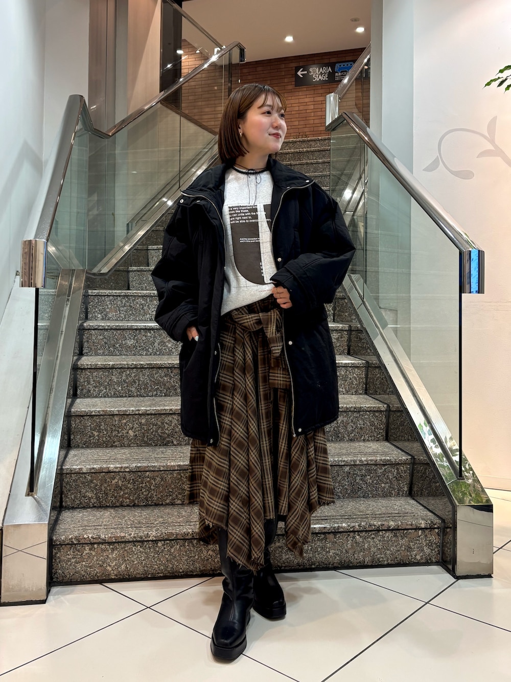 グレー系のTシャツ/カットソー、ブラウン系のスカート、ブラック系のダウンジャケット/コートを着用したレディースの冬コーディネートの3枚目の写真