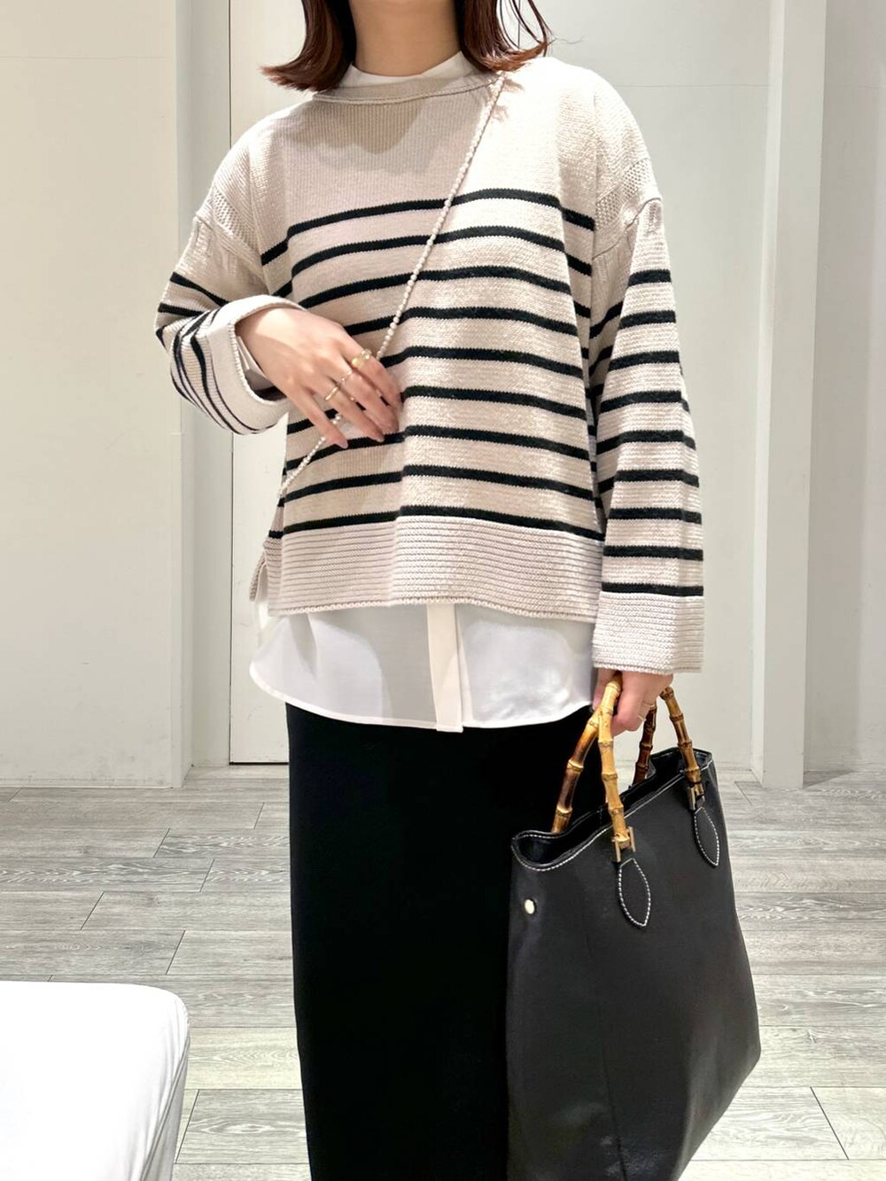 ブラック系のトートバッグ、ベージュ系のニット/セーター、ホワイト系のシャツ/ブラウスを着用したレディースの冬コーディネートの2枚目の写真