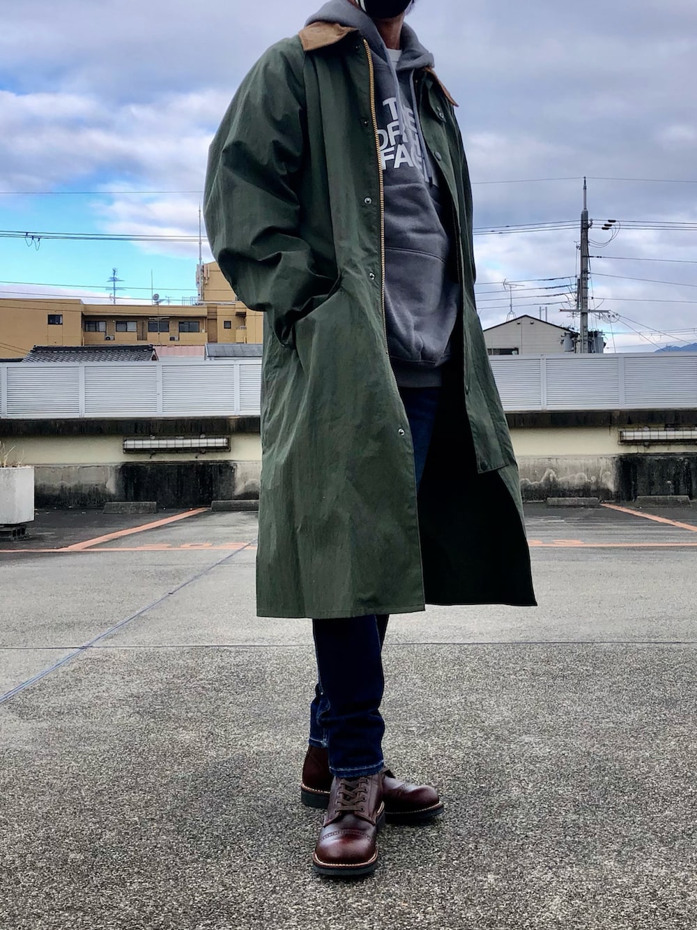 グレー系のパーカー、グリーン系のステンカラーコート、ブルー系のデニムパンツを着用したメンズの冬コーディネートの2枚目の写真