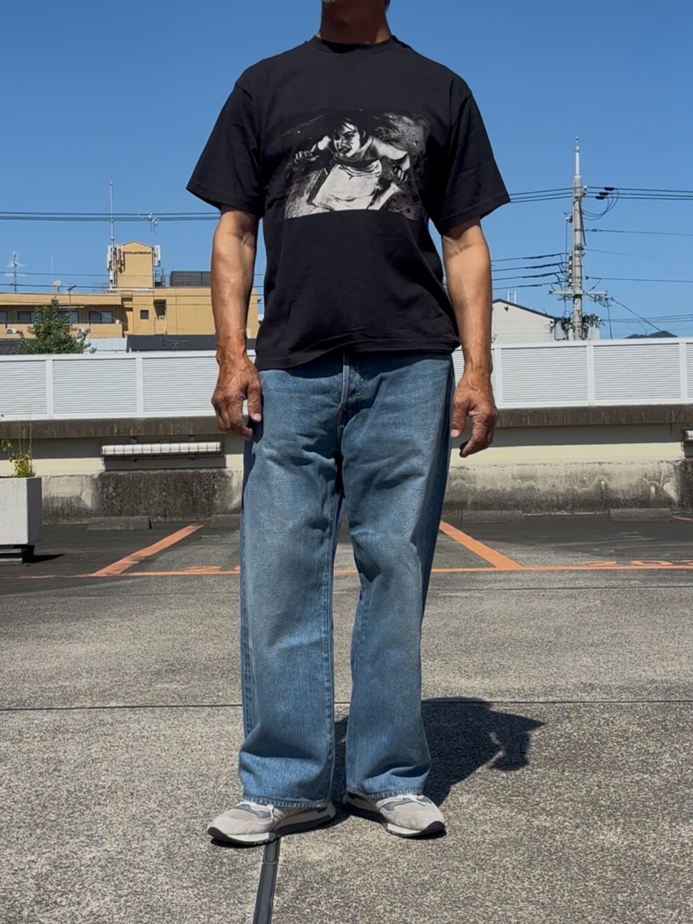 グレー系のスニーカー、ブラック系のTシャツ/カットソー、ブルー系のデニムパンツを着用したメンズの秋コーディネートの2枚目の写真
