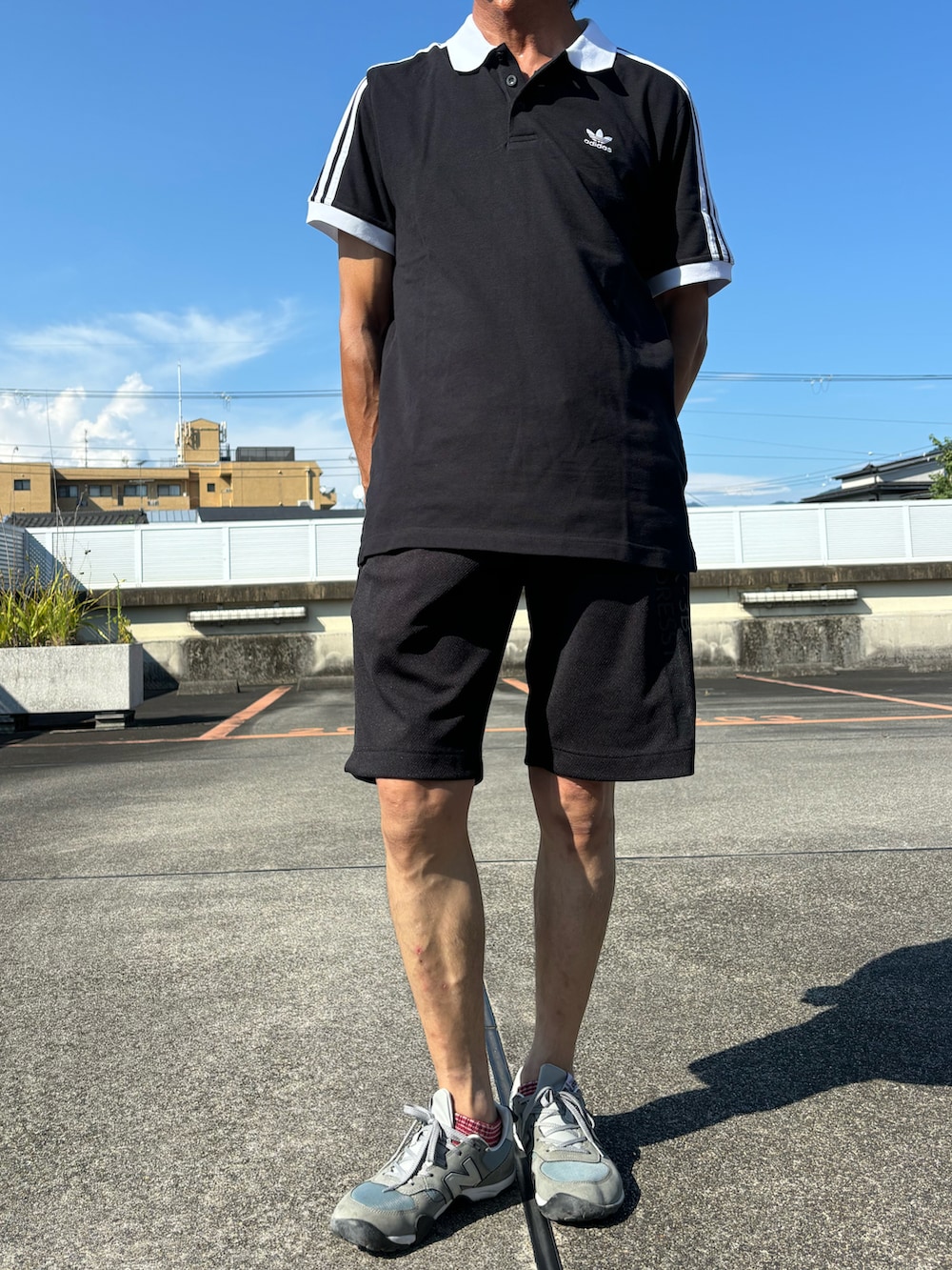 ブラック系のポロシャツ、ブラック系のその他パンツ、グレー系のスニーカーを着用したメンズの夏コーディネートの2枚目の写真