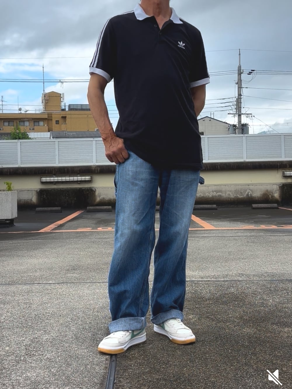 ブラック系のポロシャツ、ブルー系のデニムパンツ、ホワイト系のスニーカーを着用したメンズの夏コーディネートの2枚目の写真