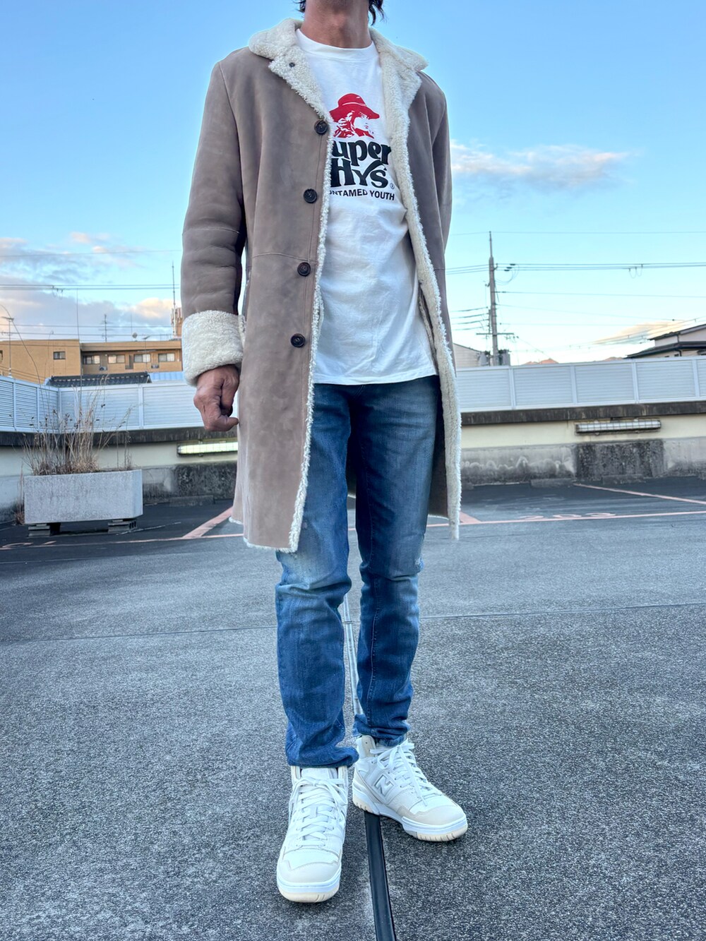 ホワイト系のTシャツ/カットソー、ブラウン系のムートンコート、ブルー系のデニムパンツを着用したメンズの冬コーディネートの2枚目の写真