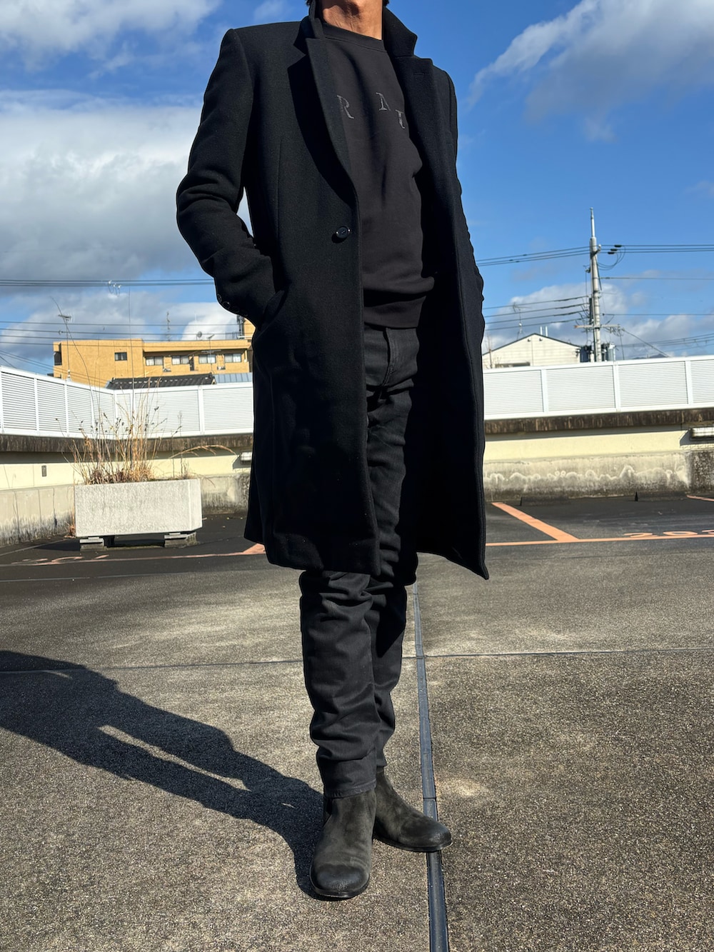 ブラック系のスウェット、ブラック系のチェスターコート、ブラック系のブーツを着用したメンズの冬コーディネートの2枚目の写真