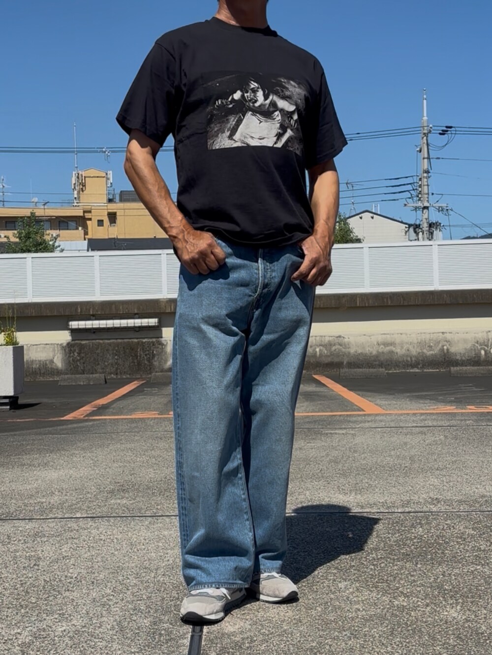 グレー系のスニーカー、ブラック系のTシャツ/カットソー、ブルー系のデニムパンツを着用したメンズの秋コーディネートの3枚目の写真