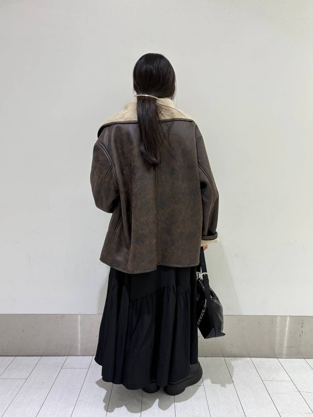 ブラウン系のムートンコート、ブラック系のショルダーバッグ、ブラック系のサンダルを着用したレディースの冬コーディネートの3枚目の写真