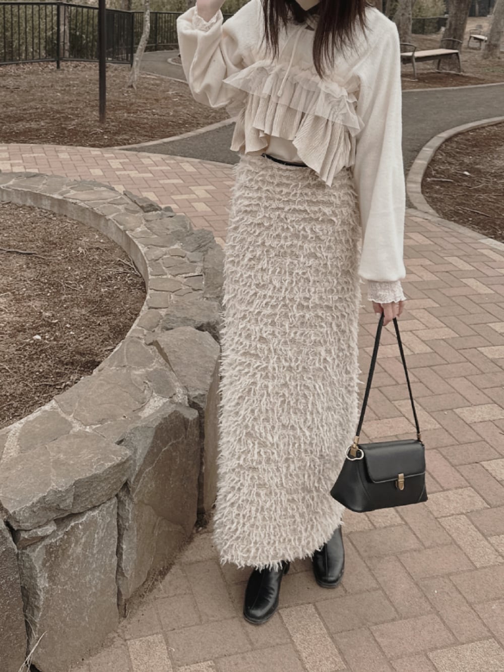 ホワイト系のニット/セーター、ベージュ系のスカート、ブラック系のブーツを着用したレディースの春コーディネートの2枚目の写真