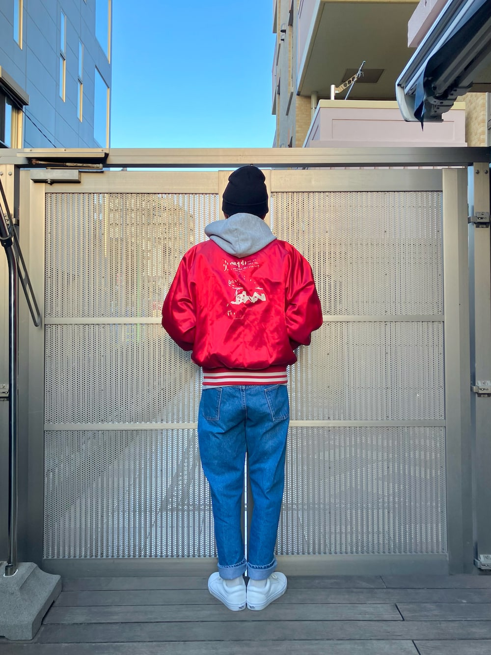 レッド系のナイロンジャケット、ブルー系のデニムパンツ、ホワイト系のスニーカーを着用したメンズの冬コーディネートの2枚目の写真