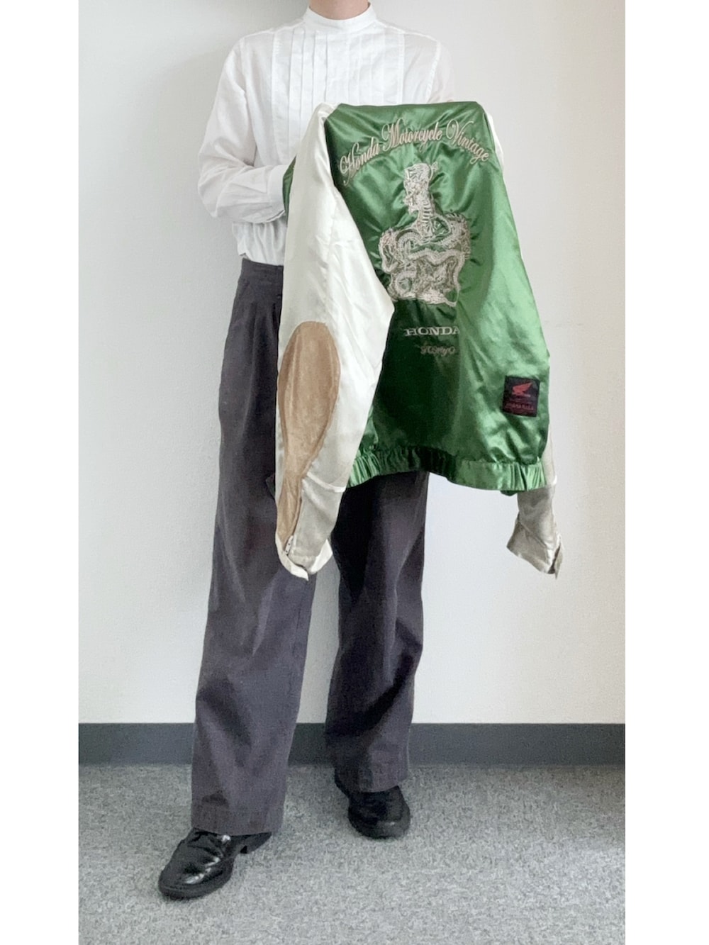 グレー系のスラックス、ブラック系のドレスシューズ、グリーン系のスカジャンを着用したメンズの春コーディネートの2枚目の写真