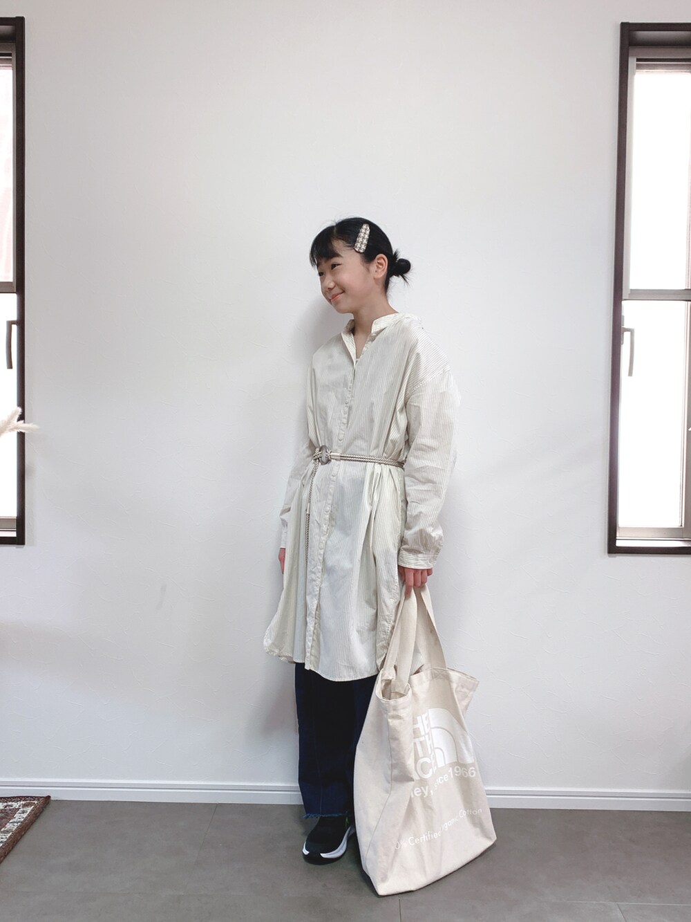 ブルー系のデニムパンツ、ベージュ系のシャツワンピース、ベージュ系のバッグを着用したキッズの春コーディネートの2枚目の写真