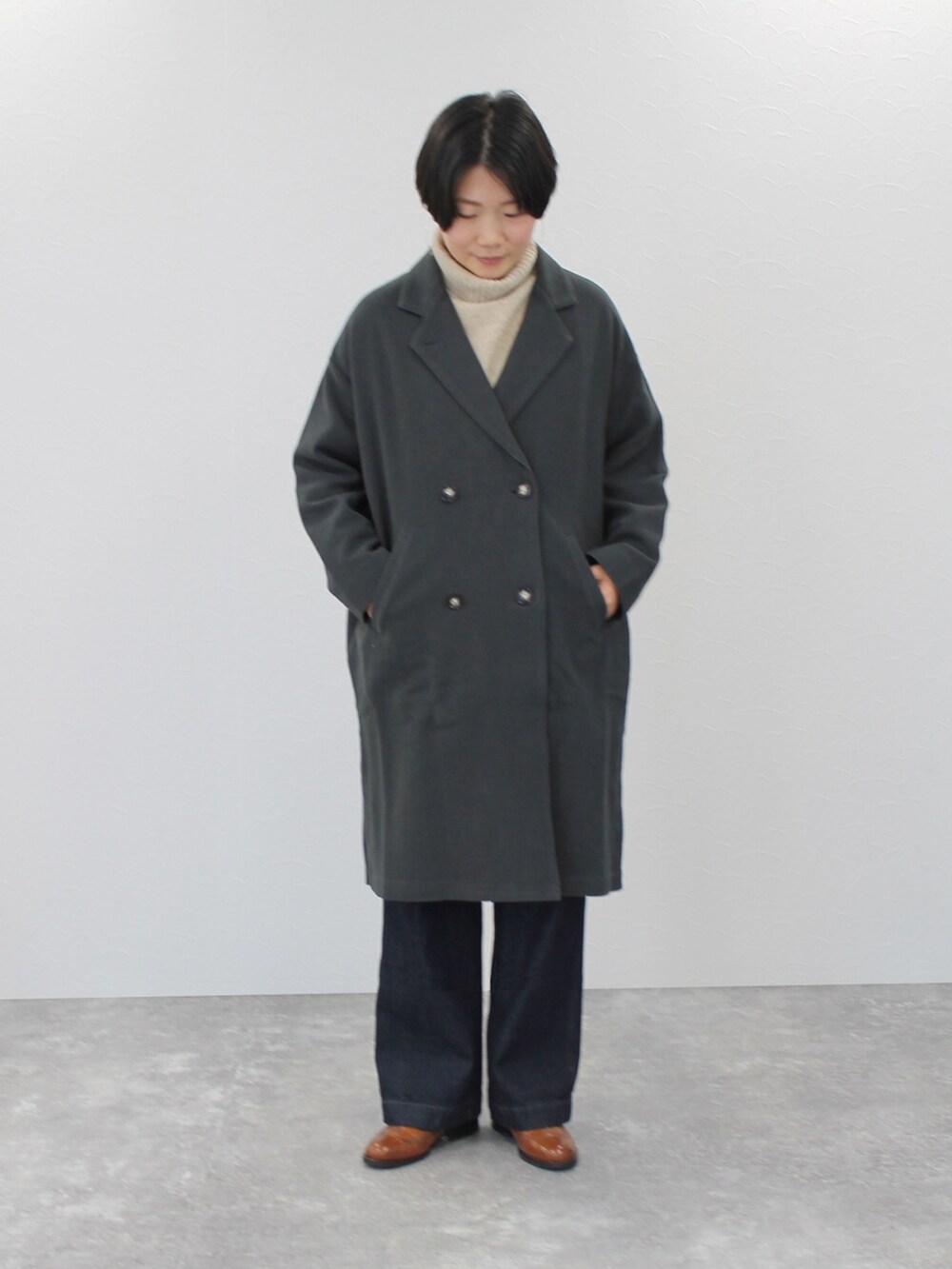 グレー系のチェスターコート、ベージュ系のニット/セーター、ブルー系のデニムパンツを着用したレディースの秋コーディネートの3枚目の写真