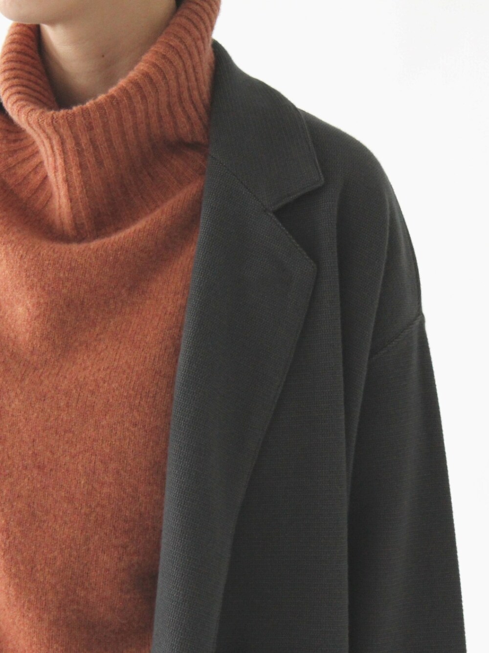 オレンジ系のニット/セーター、グレー系のチェスターコート、グレー系のスカートを着用したレディースの冬コーディネートの5枚目の写真