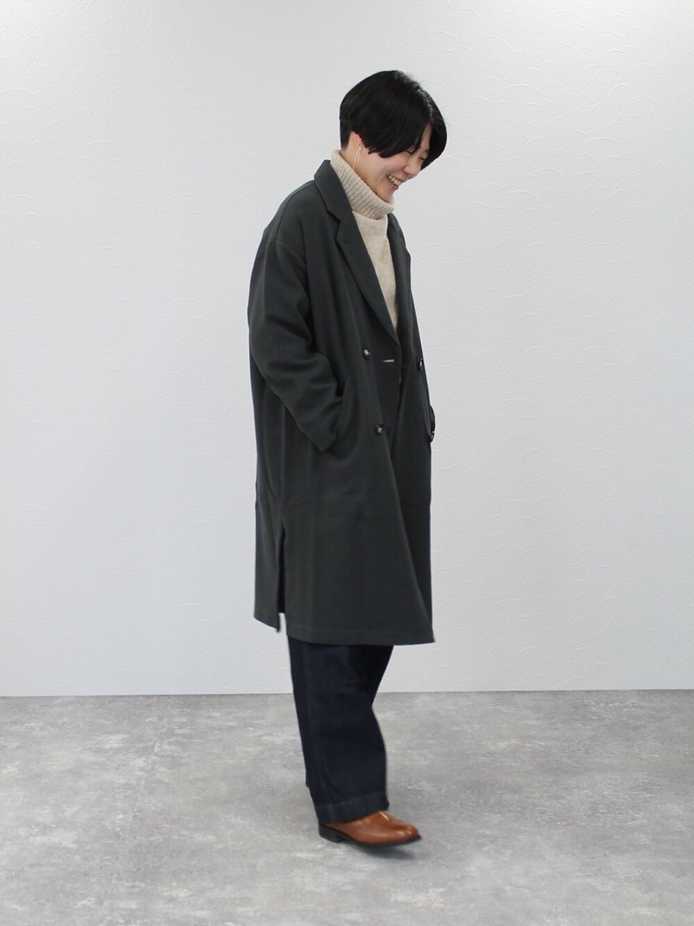 グレー系のチェスターコート、ベージュ系のニット/セーター、ブルー系のデニムパンツを着用したレディースの秋コーディネートの2枚目の写真