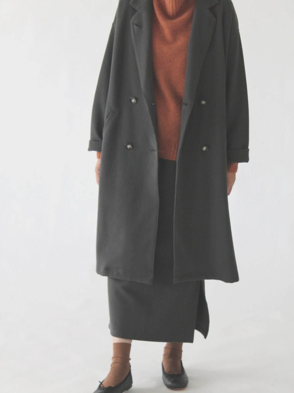 オレンジ系のニット/セーター、グレー系のチェスターコート、グレー系のスカートを着用したレディースの冬コーディネートの2枚目の写真