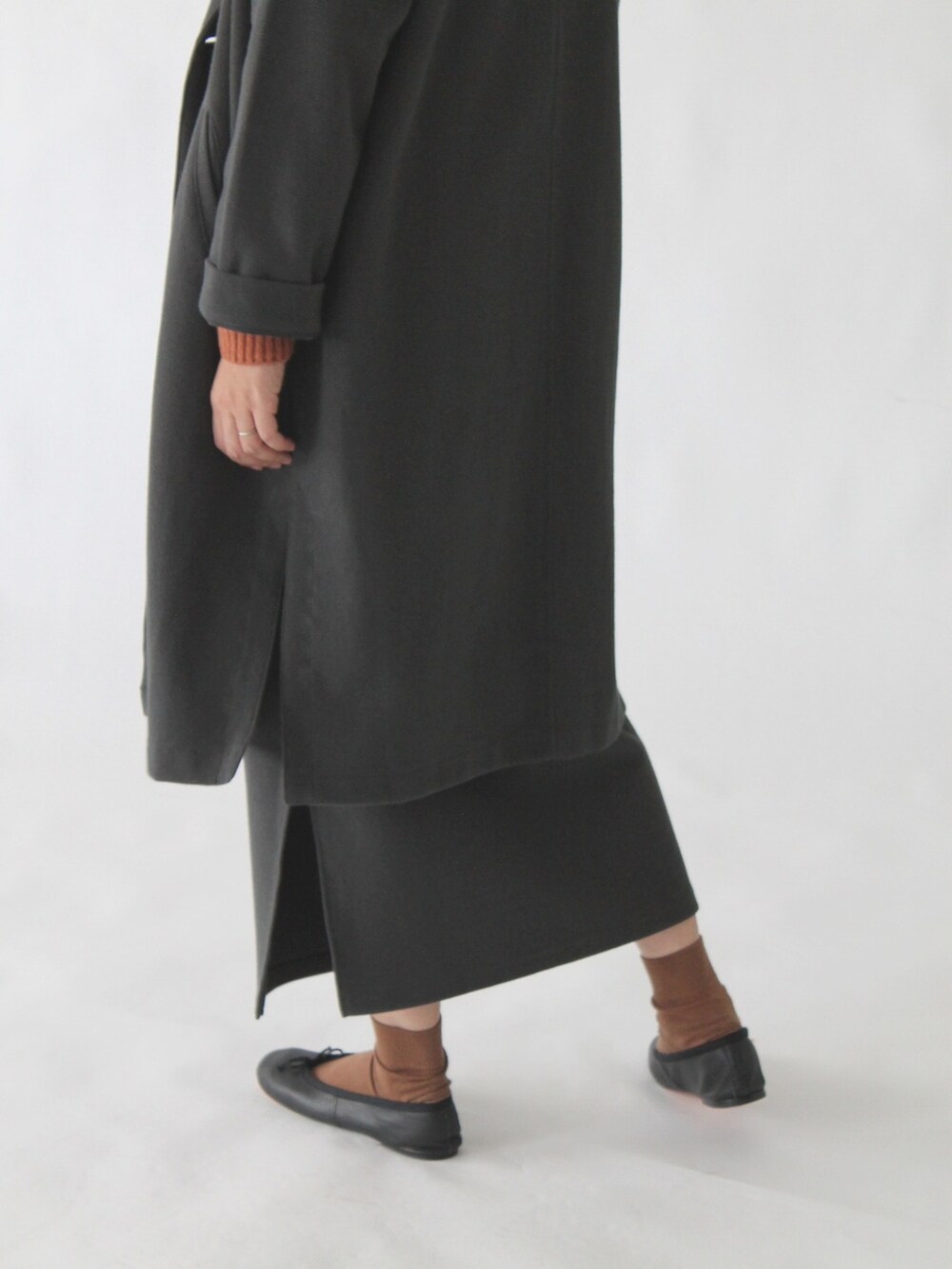 オレンジ系のニット/セーター、グレー系のチェスターコート、グレー系のスカートを着用したレディースの冬コーディネートの3枚目の写真