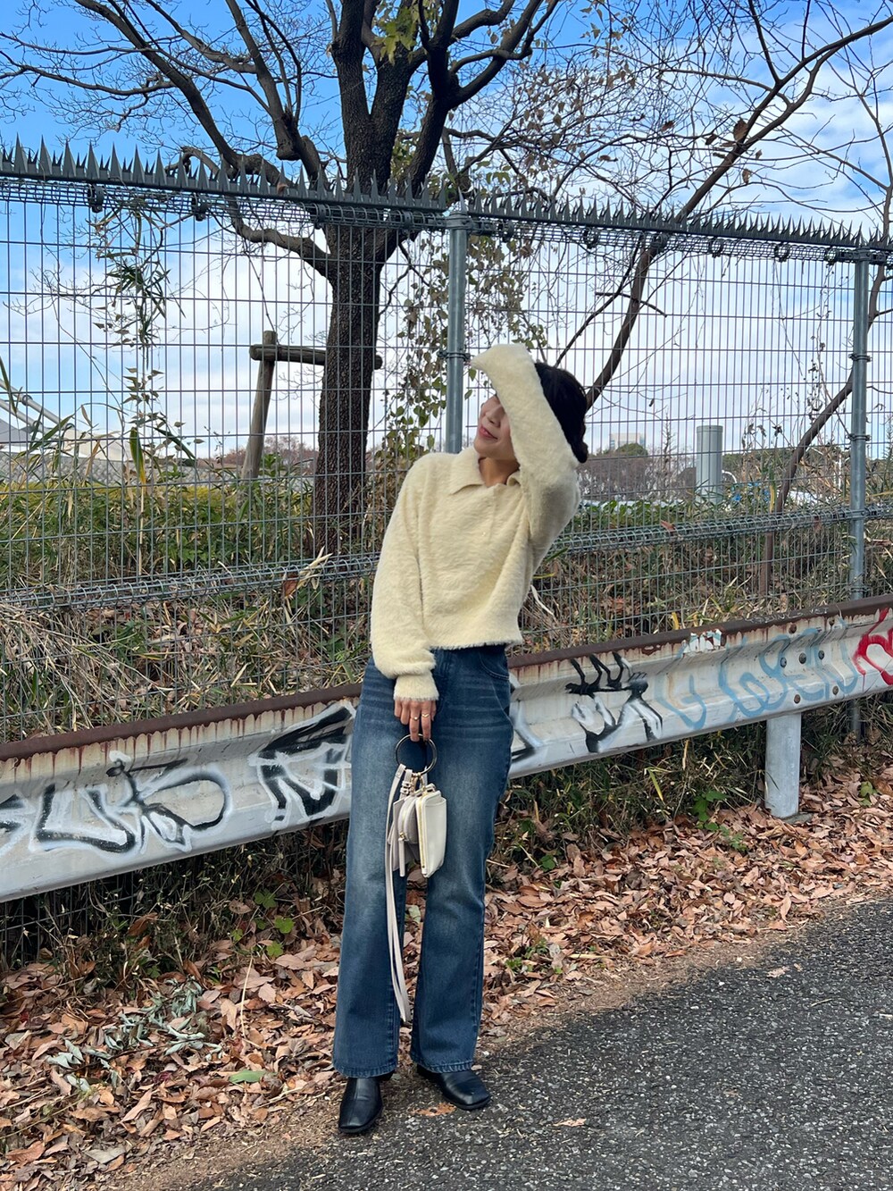 ホワイト系のニット/セーター、ブルー系のデニムパンツ、ベージュ系のショルダーバッグを着用したレディースの冬コーディネートの4枚目の写真