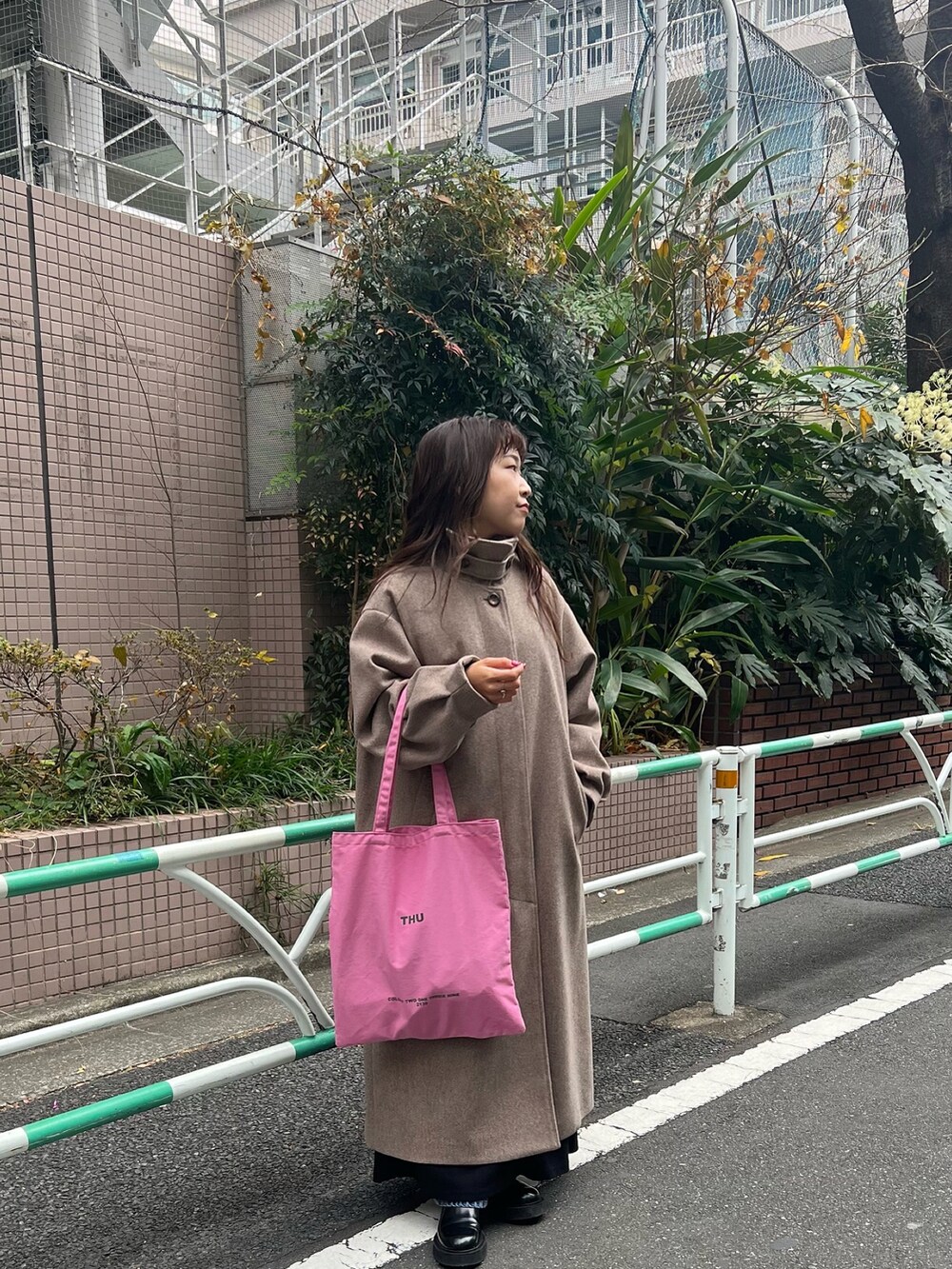 ブラウン系のステンカラーコート、ブラック系のワンピースを着用したレディースの冬コーディネートの3枚目の写真