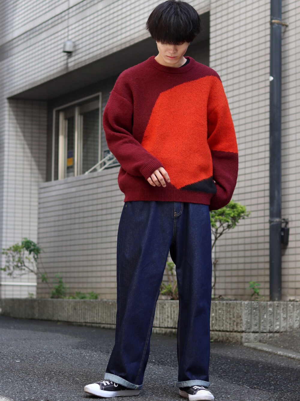レッド系のニット/セーター、ブルー系のデニムパンツ、ブラック系のスニーカーを着用したメンズの秋コーディネートの3枚目の写真