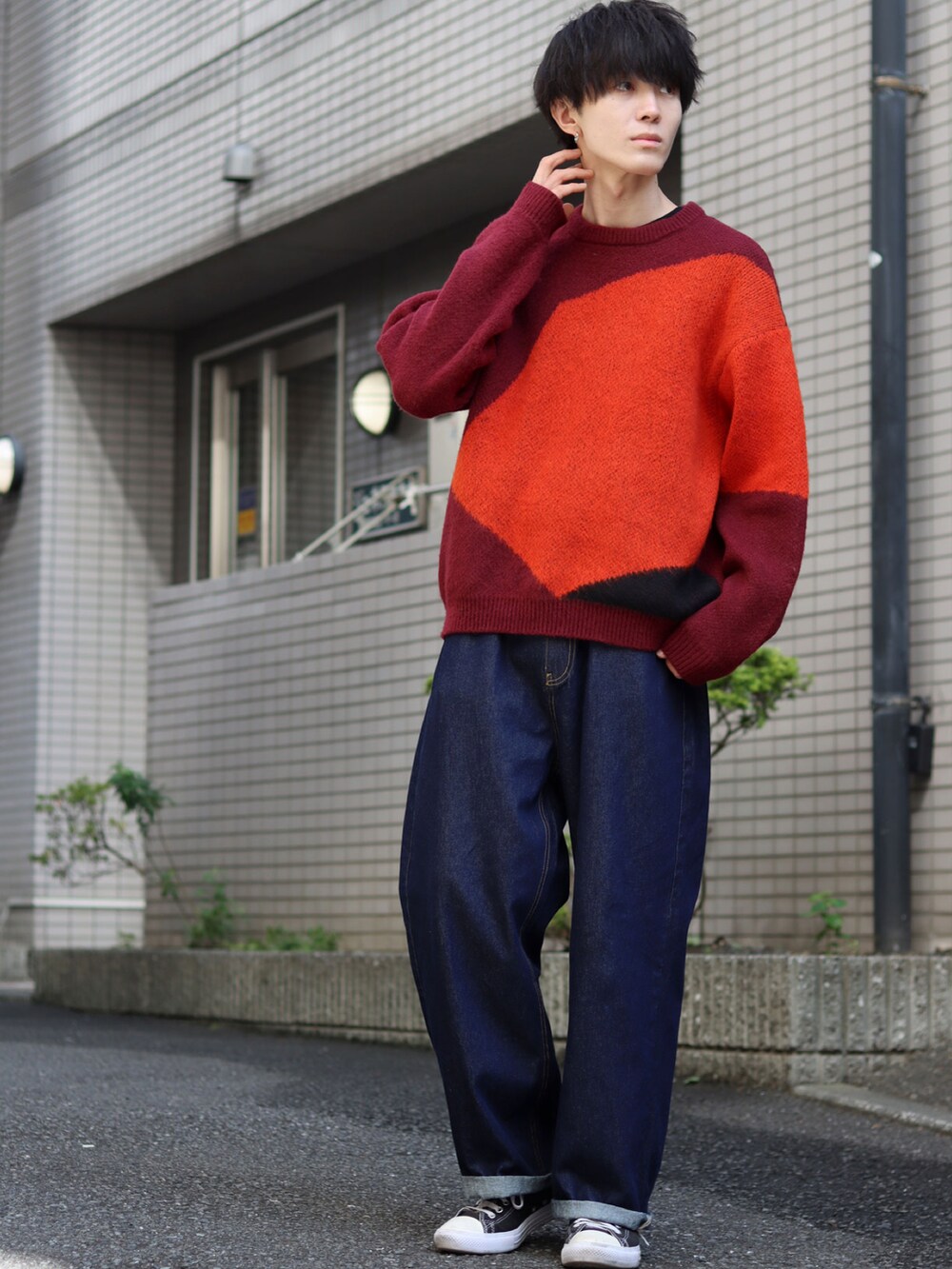 レッド系のニット/セーター、ブルー系のデニムパンツ、ブラック系のスニーカーを着用したメンズの秋コーディネートの2枚目の写真