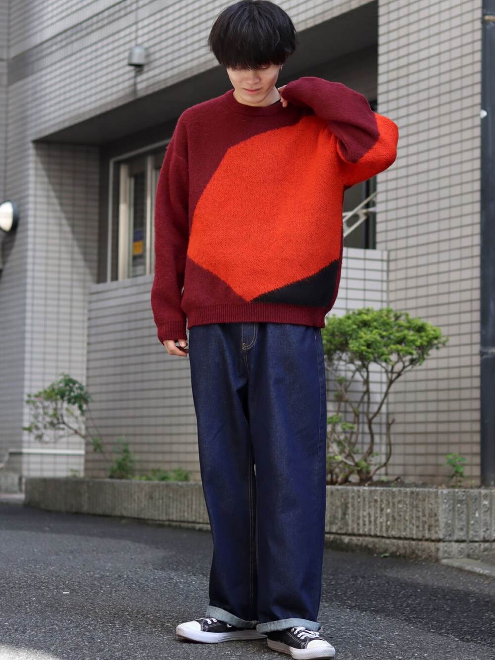 レッド系のニット/セーター、ブルー系のデニムパンツ、ブラック系のスニーカーを着用したメンズの秋コーディネートの4枚目の写真