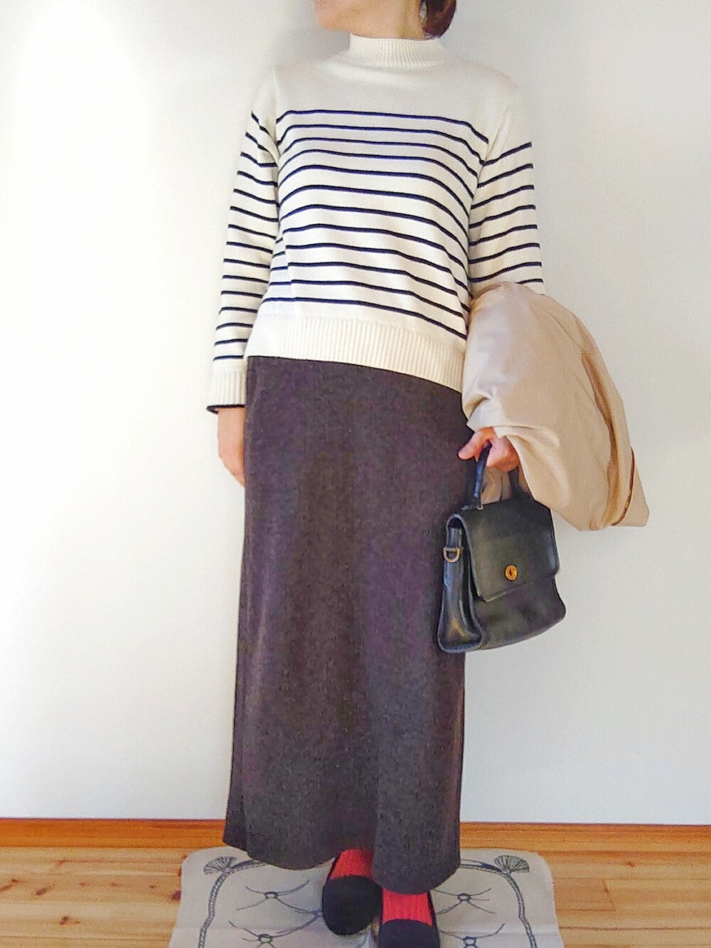 ベージュ系のステンカラーコート、ホワイト系のニット/セーター、グレー系のスカートを着用したレディースの秋コーディネートの2枚目の写真