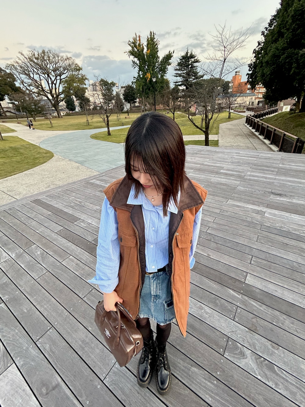 ブラウン系のボストンバッグ、ブルー系のデニムスカート、ブラック系のブーツを着用したレディースの秋コーディネートの2枚目の写真