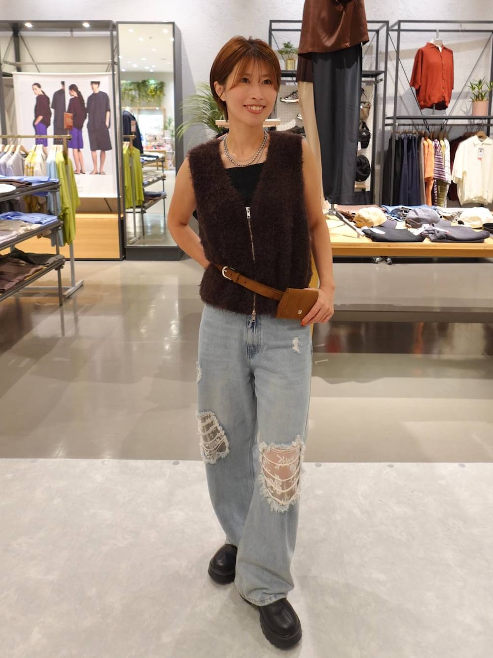 ブルー系のデニムパンツ、ブラウン系のベスト、イエロー系のベルトを着用したレディースの夏コーディネートの2枚目の写真