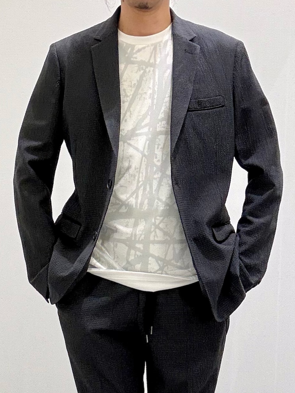 ホワイト系のTシャツ/カットソー、グレー系のテーラードジャケット、ブラック系のスリッポンを着用したメンズの春コーディネートの4枚目の写真