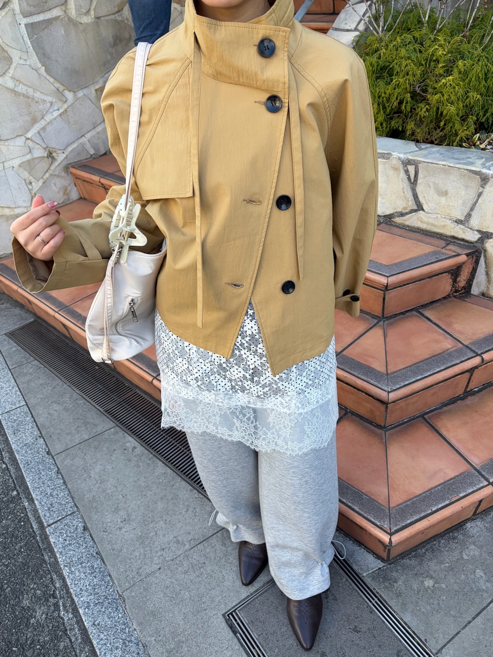 イエロー系のトレンチコート、グレー系のスウェットパンツ、ブラウン系のブーツを着用したレディースの冬コーディネートの4枚目の写真