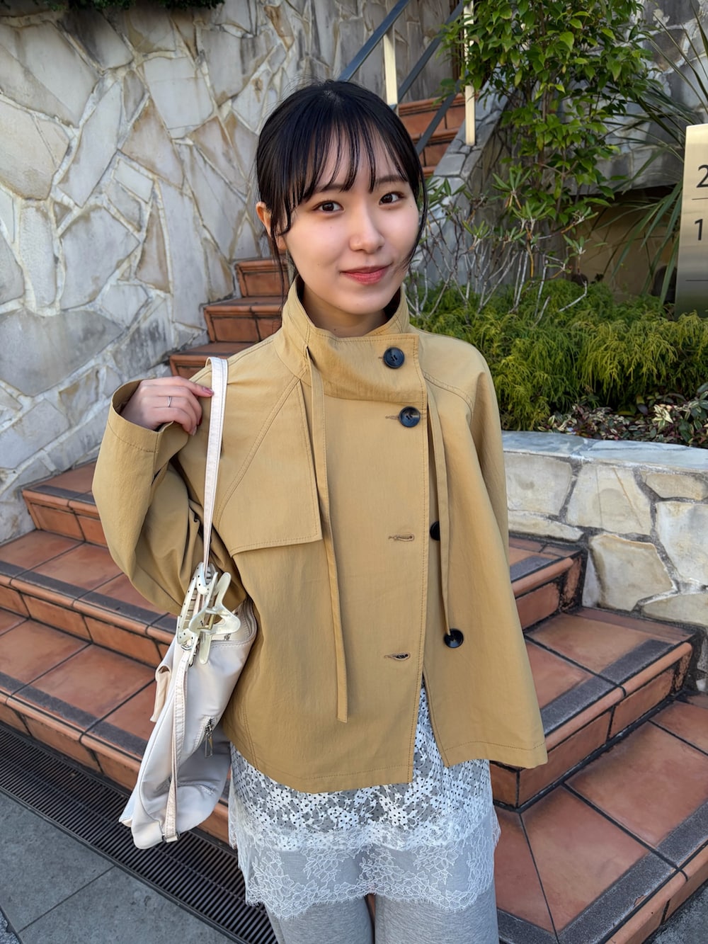 イエロー系のトレンチコート、グレー系のスウェットパンツ、ブラウン系のブーツを着用したレディースの冬コーディネートの2枚目の写真