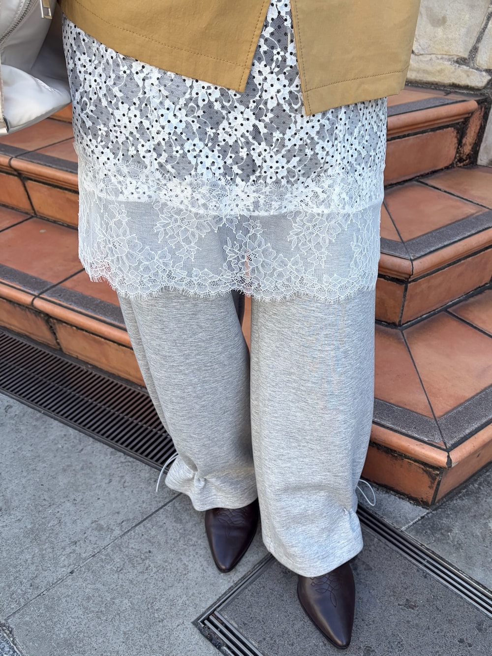 イエロー系のトレンチコート、グレー系のスウェットパンツ、ブラウン系のブーツを着用したレディースの冬コーディネートの5枚目の写真