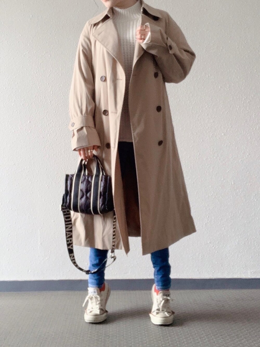 ベージュ系のトレンチコート、ホワイト系のニット/セーター、ブラック系のバッグを着用したレディースの冬コーディネートの2枚目の写真