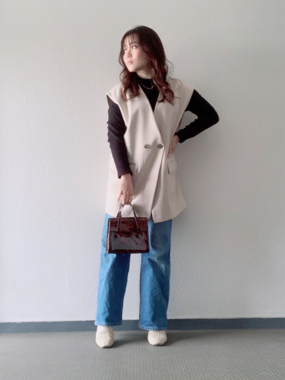 ベージュ系のベスト、ブラウン系のハンドバッグ、ブルー系のデニムパンツを着用したレディースの春コーディネートの2枚目の写真