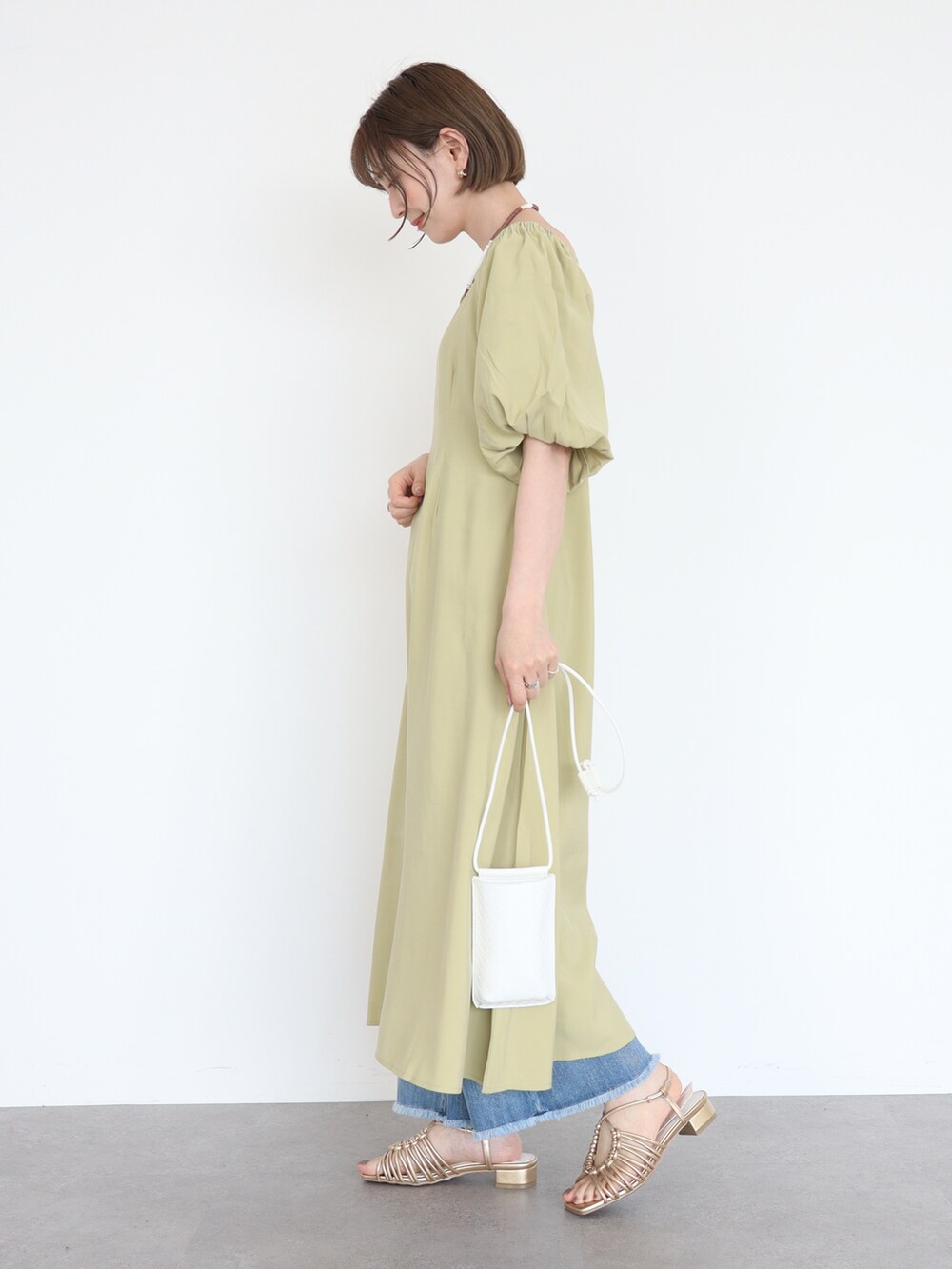 ゴールド系のサンダル、グリーン系のワンピース、ブルー系のデニムパンツを着用したレディースの春コーディネートの2枚目の写真