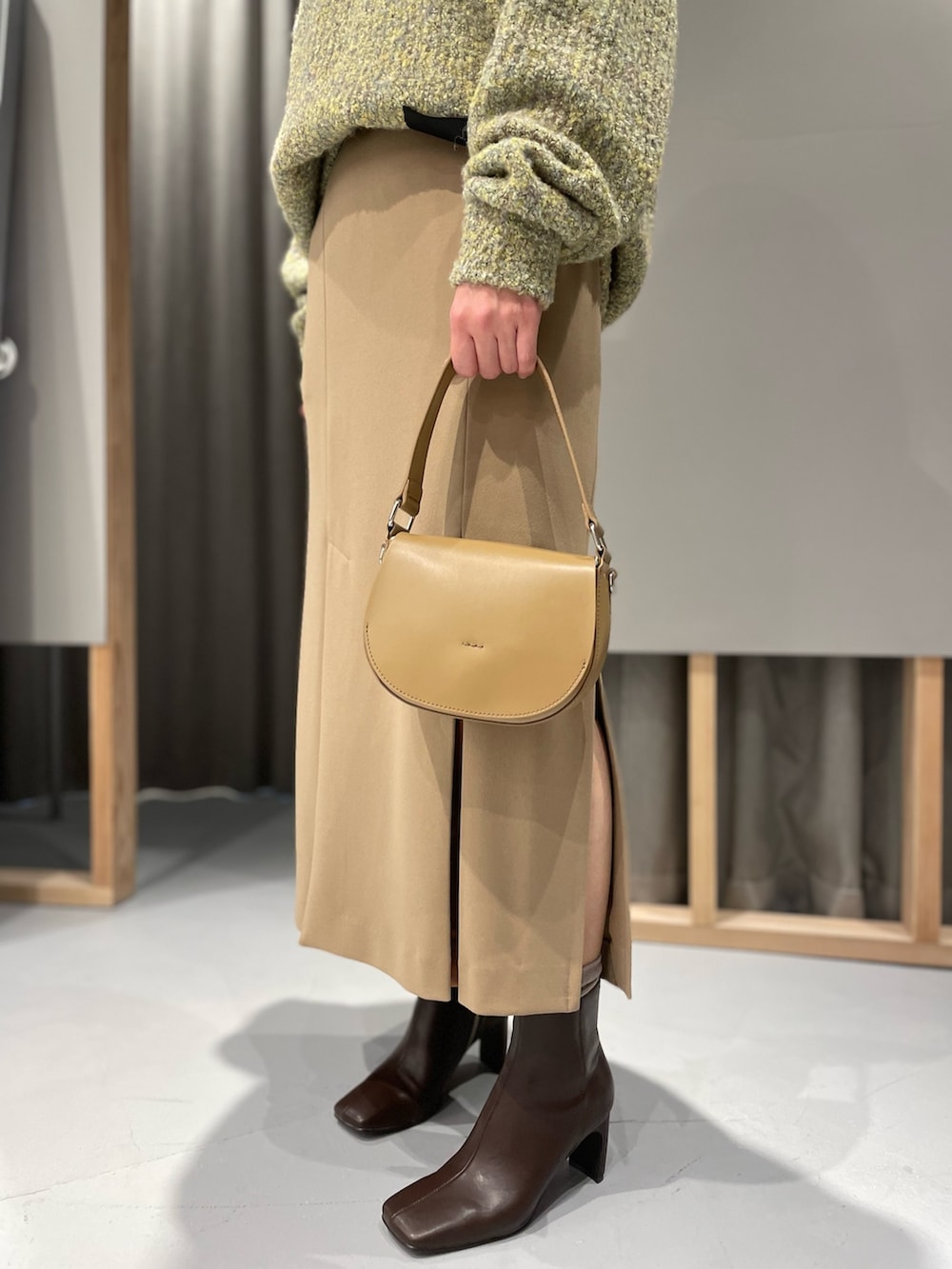 イエロー系のニット/セーター、ベージュ系のスカート、ブラウン系のブーツを着用したレディースの冬コーディネートの3枚目の写真