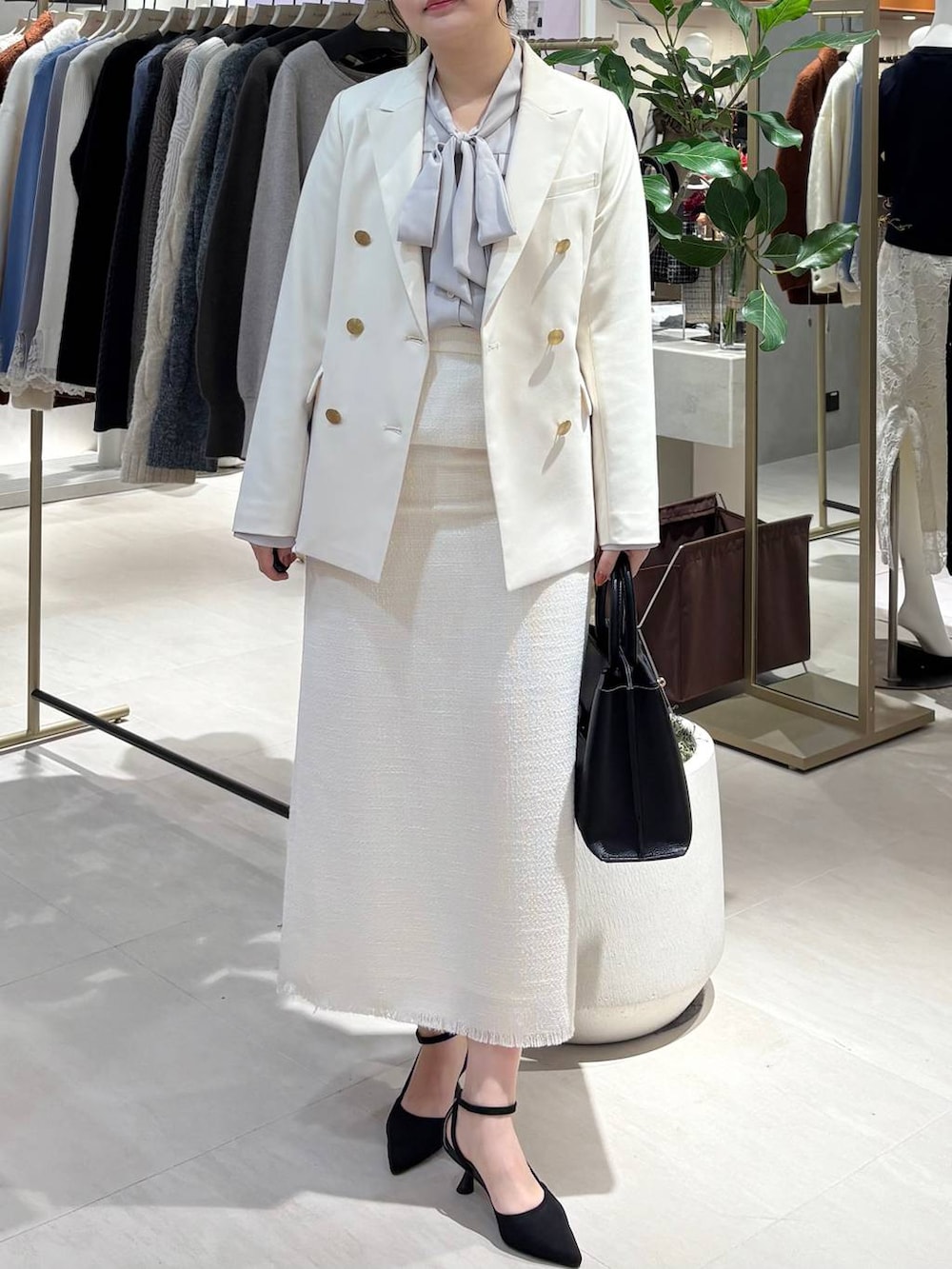 ブラック系のパンプス、ブラック系のトートバッグ、ホワイト系のテーラードジャケットを着用したレディースの春コーディネートの2枚目の写真