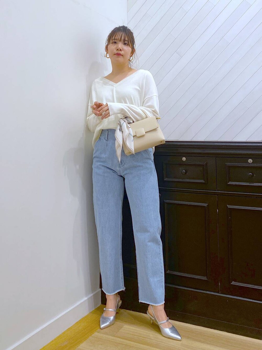 ホワイト系のハンドバッグ、ブルー系のデニムパンツ、シルバー系のサンダルを着用したレディースの春コーディネートの2枚目の写真