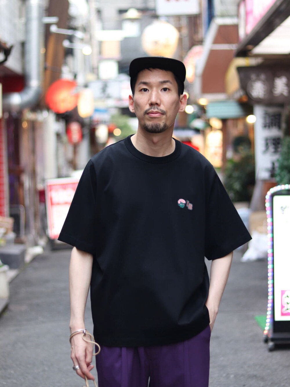 ブラック系のTシャツ/カットソー、パープル系のスラックス、ベージュ系のショルダーバッグを着用したメンズの夏コーディネートの4枚目の写真