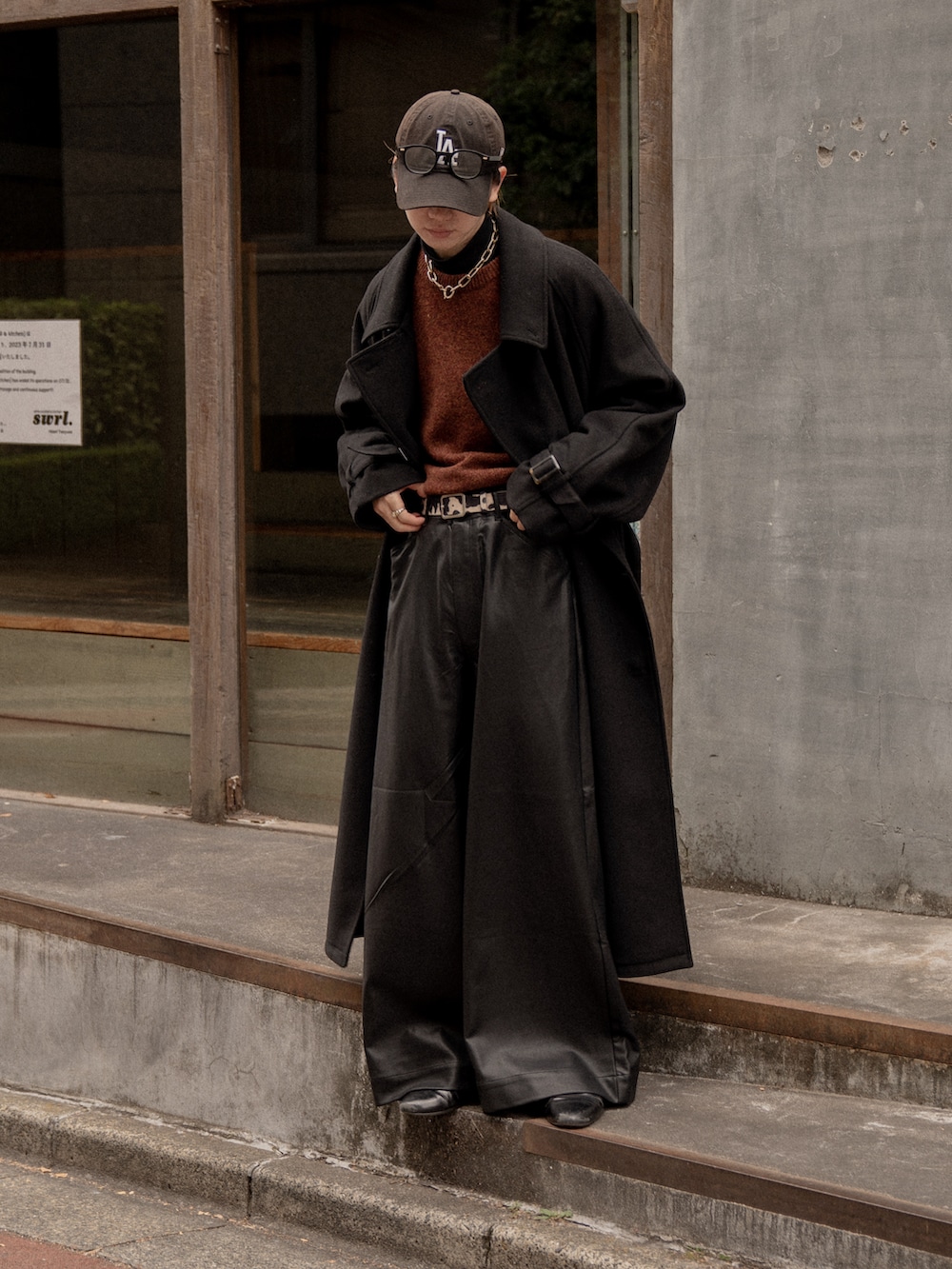 ブラック系のステンカラーコート、レッド系のニット/セーター、ブラック系のその他パンツを着用したメンズの冬コーディネートの3枚目の写真