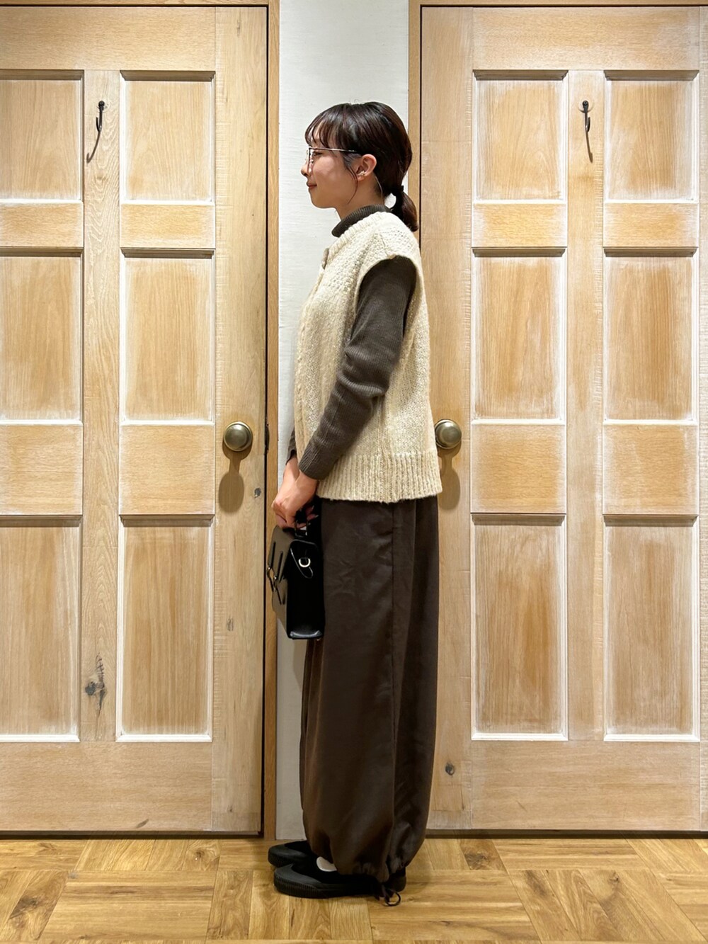 ホワイト系のベスト、ブラウン系のニット/セーター、ブラック系のハンドバッグを着用したレディースの冬コーディネートの2枚目の写真